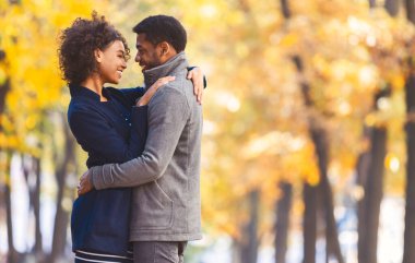 Aşk ve aşk kavramı. Tatlı siyah çift sarılıyor ve birbirlerine bakıyor, sonbahar ağaçları arka planda, fotokopi alanı olan panorama