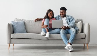 Genç, Afro-Amerikalı çifti severken, video izlerken, fotoğraflarına bakarken ya da ne alacaklarını seçerken, oturma odasında kanepede oturup dinlenirken. Kadını kucaklayan adam, bedava kopya alanı.