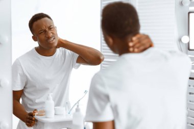 Boynu ağrıyan Afrikalı adam sabahları acı çekiyor, evdeki banyoda aynanın yanında duruyor. Erkek sağlık sorunları, boyun ağrısı, kötü duruş ve baş ağrısı sorunları. Seçici Odaklanma