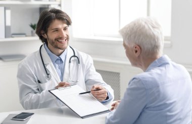 Dost canlısı bir yaşlı doktor klinikteki yaşlı kadın hastaya reçete yazıyor.