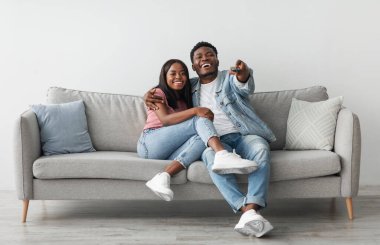 Güzel Afro-Amerikalı çift oturma odasındaki kanepede dinleniyor, gülümseyen adam ve kadın birlikte vakit geçiriyorlar, televizyon ya da film izliyorlar, kucaklaşıyorlar, uzaktan kumandayla gülüyorlar.