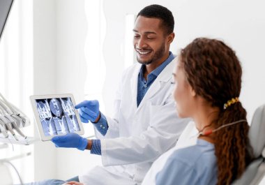 Siyahi erkek dişçi ve kadın hasta klinikteki dijital tablette röntgen fotoğrafına bakıyorlar.