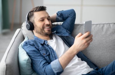Rahatlama zamanı. Kablosuz kulaklıklı yakışıklı, sakallı adam akıllı telefondan müzik dinliyor, fotokopi çekiyor, yakın plan çekiyor. Kulaklıklı mutlu adam cep telefonundan video izliyor.