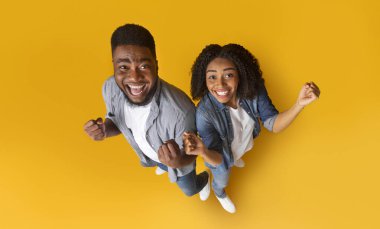 Büyük şans. Heyecanlı siyahi çiftin başarıyı veya zaferi kutlarken ellerini kaldırması, sarı arka planda duran yumruklarını sıkması.