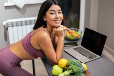 İnce Çinli kadın dizüstü bilgisayar kullanıyor ve internette yemek tarifi arıyor. Evdeki mutfakta yemek hazırlıyor. Kilo Verme, Sağlıklı Yeme ve Yaşam Tarzı Konsepti