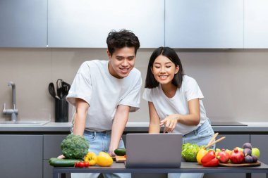 Asyalı çiftler birlikte yemek pişiriyor. İnternette yemek tarifi arıyorlar. Evde mutfakta yemek hazırlıyorlar. Hafta sonu tatili, aile beslenmesi, aşçılık sitesi konsepti. Seçici Odaklanma