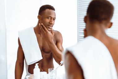 Modern banyoda Tüysüz Ayna Yanı Başında Tıraş olduktan sonra Yumuşak Yüze Dokunan Çekici Afro-Amerikan Adam. Erkek Yüz Cilt Rutini. Seçici odak