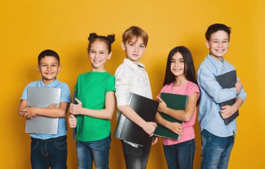 Okul çocukları ile satır ayakta ve kameraya sarı arka plan üzerinde seyir defter,