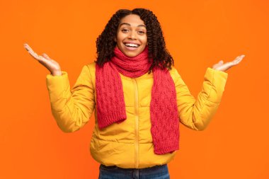 Sarı Stüdyo 'nun arka planında duran, kışlık ceket ve eşarp takan, Joy Gesturing' deki kameraya bakan heyecanlı siyah kadın. Pozitif İnsanlar Duygu, Heyecan Konsepti