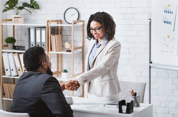 Черный нанимающий менеджер пожимает руку успешному кандидату на вакансию после собеседования в современном офисе, копирует пространство