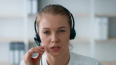 Kulaklık takan genç bir kadın, çağdaş bir ofis ortamında ciddi bir sohbete girişiyor. Kurumsal ortam, onun profesyonelliğini ve işine olan bağlılığını vurguluyor..