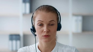 Kulaklık takmış genç beyaz bir kadın yoğun bir gündüz vakti iş yerinde mesleki bir yaşam tarzını sergiliyor..