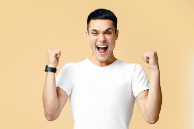 Gerçekten etkileyici başarılar, kazanma dansı, ödüllendirme, olumlu haberler. Başarılı genç adam bağırıyor, ellerini kaldırıyor zaferi kutluyor, arka planda izole edilmiş, boş alan, stüdyo çekimi