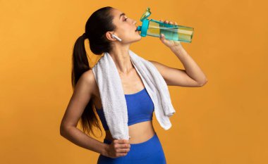 Fitness ve Sağlıklı Yaşam Konsepti. Spor salonunda spor salonunda idmandan sonra mineral suyu içen kulaklık takıp pankart takan genç bir kadının portresi. Sağlık ve Eğitim