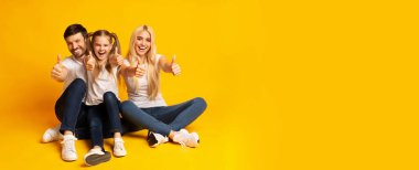 Gibi. Heyecanlı Aile Gesturing Thumbs Up Kamera Sarı Arka Plan Üzerinde Katta Oturan Bakarak. Stüdyo Çekimi