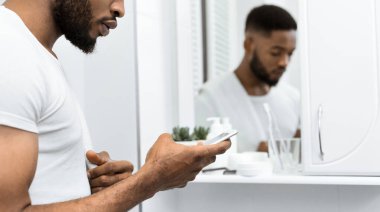 Yakışıklı afro adam banyoda akıllı telefon mesajı okuyor. Banyoda adam konsepti