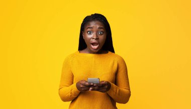 Şok olmuş Afrikalı Amerikalı Kadın Akıllı Telefon, Cep Telefonu Teklifine Duygusal Tepki, Cep Telefonu Şaşkınlıkla Ağzını Açan Siyah Kadın, Stüdyoda Sarı Arkaplanda Duran, Boşluğu Kopyala