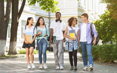 Mutlu üniversite öğrencileri kampüste birlikte yürüyor, teneffüste sohbet ediyor ve gülüyorlar, kopyalama alanı.