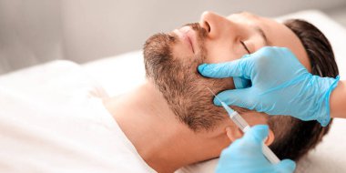 Kozmetik uzmanı klinikteki yakışıklı adam için yaşlanma önleyici prosedür hazırlayan mavi lastik eldivenleri verdi. Sakallı orta yaşlı adam güzellik salonunda güzellik iğnesi yaptırıyor.