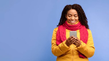 Sosyal Medya Mobil Uygulamalarında Akıllı Telefon Ağı Kullanan Afrikalı Amerikalı Kadın Mor Stüdyo Arkaplanının Üzerinde Kışlık Kıyafetler Giyiyor. Cep telefonu Uygulaması Konsepti