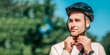 Şehirde bisiklete binmek için hazırlık. Tişörtlü yakışıklı genç adam kaskını takıyor, kapalı, açık havada, boş alanda.