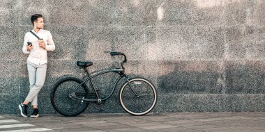 Genç bir adam, şık bisikleti yakınlarda dinlenirken akıllı telefonunu rastgele tutarak beton dokuma duvara yaslanıyor. Bu canlı cadde, şehir manzarasında bin yıllık bir yaşam tarzını yakalıyor, uzayı taklit ediyor.