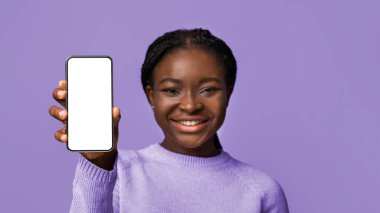 Harika bir uygulama. Mor arka planda izole edilmiş güzel Afrikalı Amerikalı kadının elinde siyah ekranlı modern akıllı telefonun tasarımı, seçici odak noktası, kopyalama alanı.