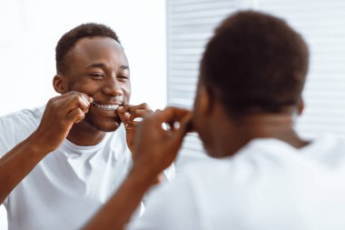 Diş ipi kullanan, diş ipi kullanan, diş ipi kullanan, dişlerini temizleyen, dişlerini fırçalayan, dişlerini fırçalayan Afrikalı bir adam. Diş sigortası ve sağlıklı ağız sağlığı konsepti. Seçici Odaklanma