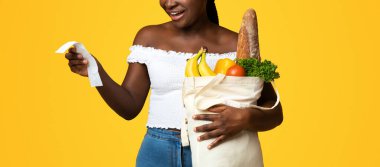 Alışveriş Ekonomisi. Paket dolusu yiyecek ve makbuz taşıyan, çantalarını taşıyan, sarı stüdyonun arka planında duran, fotokopi çeken, çantalarını dolduran,