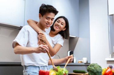 Birlikte yemek pişirmek. Modern mutfaktaki yemek için salata pişirirken Asyalı eşe sarılmak. Eşler hafta sonları yemek hazırlıklarının keyfini çıkarıyorlar. Aile Beslenme ve Tarifleri