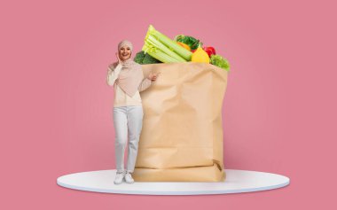 Bir müşteri, markette içi taze sebze ve meyve dolu büyük bir kese kağıdının yanında mutlu bir şekilde el kol hareketi yapar. Bu durum, bugünün pazar ortamında alışverişin kolaylığını yansıtıyor.