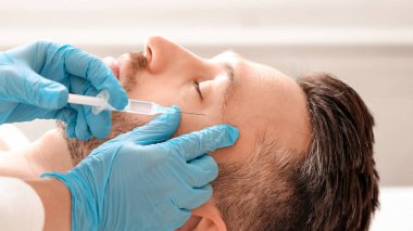 Kozmetik uzmanı estetik kliniğinde orta yaşlı yakışıklı bir adam için göz kaldırma işlemi yapıyor. Adam tanınmayan estetik cerrahın göz kırışıklıklarına güzellik iğnesi yaptırıyor.