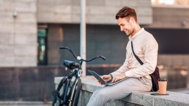 Dışarıda çalışan serbest çalışan biri. Kablosuz kulaklıklı gülümseyen adam dizüstü bilgisayarında kahve fincanı olan, uzay kopyalayan.