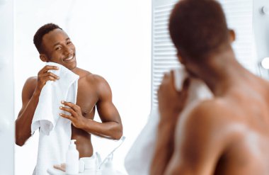 Sabahları banyoda aynanın yanında, yüzünü yıkadıktan ve tıraş olduktan sonra yüzünü havluyla silen yakışıklı Afro-Amerikan bir adam. Erkek Yüz Cilt Rutini. Seçici Odaklanma