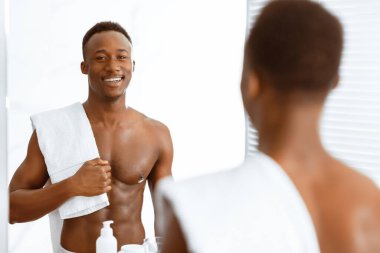 Çekici Gömleksiz Afrikalı Adam Havluyla modern banyoda dikiliyor ve yansımasına bakıyor. Erkek ÖzBakımı, Sabah Güzelliği Konsepti. Seçici Odaklanma