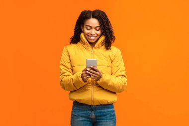 Sarı Stüdyo 'nun arkasında duran, kalın kışlık kıyafetler giyen akıllı telefonlu Afrikalı Amerikalı kadın. Cep Telefonu Kullanıcı Cep Telefonu Uygulaması Kullanımı Konsepti