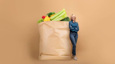 Taze sebze ve meyvelerle dolu büyük bir kesekağıdının yanında duran bir müşteri, yeni normal market alışverişini sergiliyor. Bu durum, uzaktan teslimat ve münferit satın alma eğilimlerini yansıtıyor.