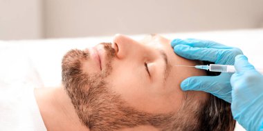 Güzellik uzmanı estetik kliniğinde orta yaşlı yakışıklı bir adam için yüz gerdirme prosedürleri yapıyor. Adam tanınmayan estetik cerrahın alnına güzellik iğnesi yaptırıyor.