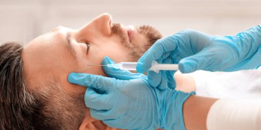 Estetik kliniğinde orta yaşlı yakışıklı bir adama güzellik iğnesi yapıyor. Adam tanınmayan plastik cerrahın göz kırışıklıklarına karşı kaldırma prosedürü uyguluyor.