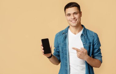Harika mobil uygulama, nakit para ve sosyal ağlar. Gülümseyen genç adam kameraya bakıyor ve boş alanı olan bir telefon gösteriyor, arka planda izole edilmiş, stüdyo çekimi, boş alan.