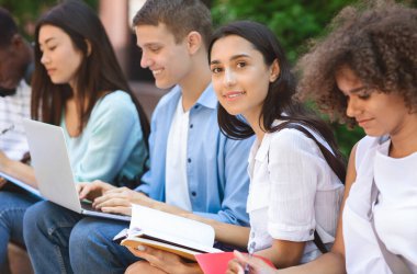 Sınavlar Hazırlık. Çok ırklı öğrencilerden oluşan bir grup açık havada birlikte çalışıyor, Notepad ile seçici olarak Arap Kız 'a odaklanıyor