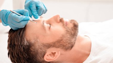 Güzellik salonunda orta yaşlı yakışıklı bir adam için yüz temizleme prosedürü. Sakallı başarılı iş adamı gözleri kapalı dinlenirken güzellik uzmanları kaplıcada siyah kafalarını yüzlerine vuruyorlar.