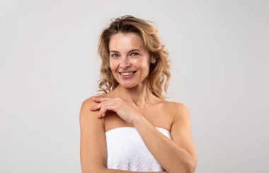 Portrait Of Pretty Middle Aged Female Wrapped In Bath Towel Posing Over Light Grey Background, Attractive Woman With Beautiful Skin Smiling At Camera, Enjoying Self-Care Treatments, Copy Space