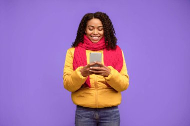 Neşeli Afro-Amerikalı Kız İnternet 'te Mesaj Kullanıyor Kış Giysileri Giyiyor Mavi Arkaplanda Stüdyoda. Mobil Uygulama Kavramı