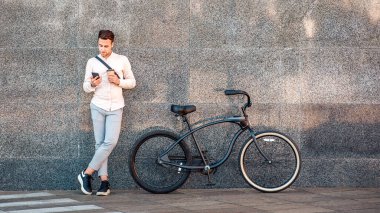 Çevrimiçi açık hava. Bisikletli ve kahveli bir iş adamı, işten çıkarken duvara yaslanan akıllı telefona bakar, boşluğu kopyalardı.