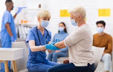 Covid-19 Aşılama. Kıdemli hasta kadın Coronavirus aşısı oluyor. Hastanede doktorla oturuyor, maske takıyor. Corona Virüs Aşısını Yaşlı Kadın 'a Hemşire İğnesi