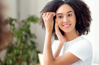 Aynanın ve güzellik prosedürünün önündeki kaş şekillerini düzeltiyorum. Binlerce yıllık neşeli Afro-Amerikan kadın saçlarını yoluyor ve sabahları banyonun iç kısımlarına bakıyor.