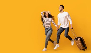 Seyahat reklamı. Çantalı ve sarı arka plandaki fotokopi alanına bakan heyecanlı genç Orta Doğulu çift, valiz taşıyan neşeli Arap eşler, tatil gezisine hazır, panorama...