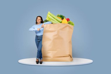 Bir müşteri gururla taze sebze ve meyve dolu büyük bir kesekağıdının yanında durur. Dekor, yeni normal bir yaşam tarzının ortasında modern bir market alışverişi deneyimini vurguluyor..