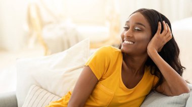 Genç Afrikalı Amerikalı bayan evde tembelce hafta sonunun keyfini çıkarıyor, oturma odasında kanepede dinleniyor. Güzel siyah kadın izinli, rahat koltukta dinleniyor, huzurlu ve mutlu hissediyor.